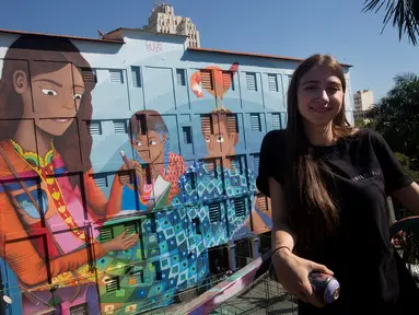 Seniman Brasil, Luna Buschinelli berpose dengan latar belakang mural berjudul 'Contos' di dinding gedung sekolah Rio de Janeiro, (19/6). Karya gadis 19 tahun itu memecahkan rekor dunia sebagai mural terbesar yang dibuat oleh wanita. (AP/Silvia Izquierdo)