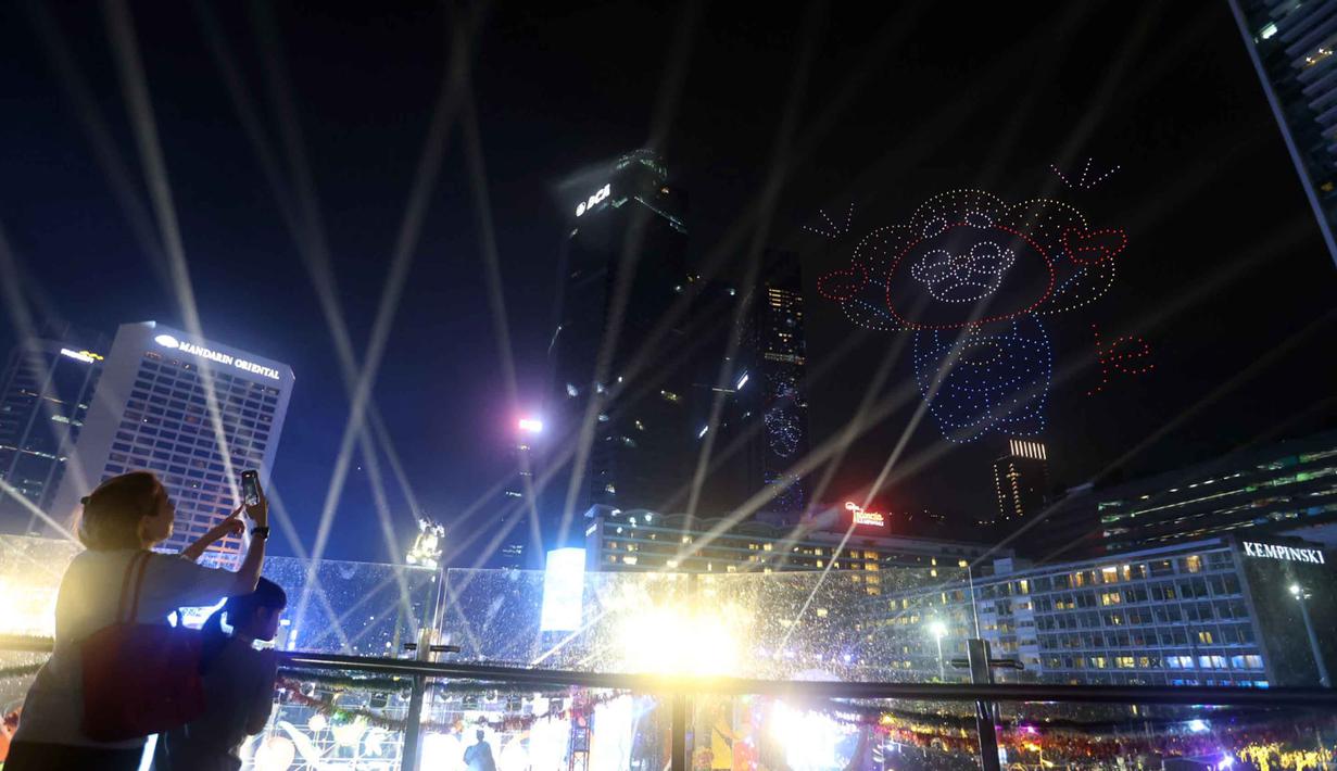 Warga yang memadati area Bundaran Hotel Indonesia, Jakarta, menengadah untuk mengabadikan momen tersebut menggunakan ponsel mereka. Tampak dalam foto, warga mengabadikan pertunjukan drone saat perayaan malam pergantian tahun di kawasan Bundaran Hotel Indonesia, Jakarta, Rabu (31/12/2025). (Kapanlagi.com/Budy Santoso)