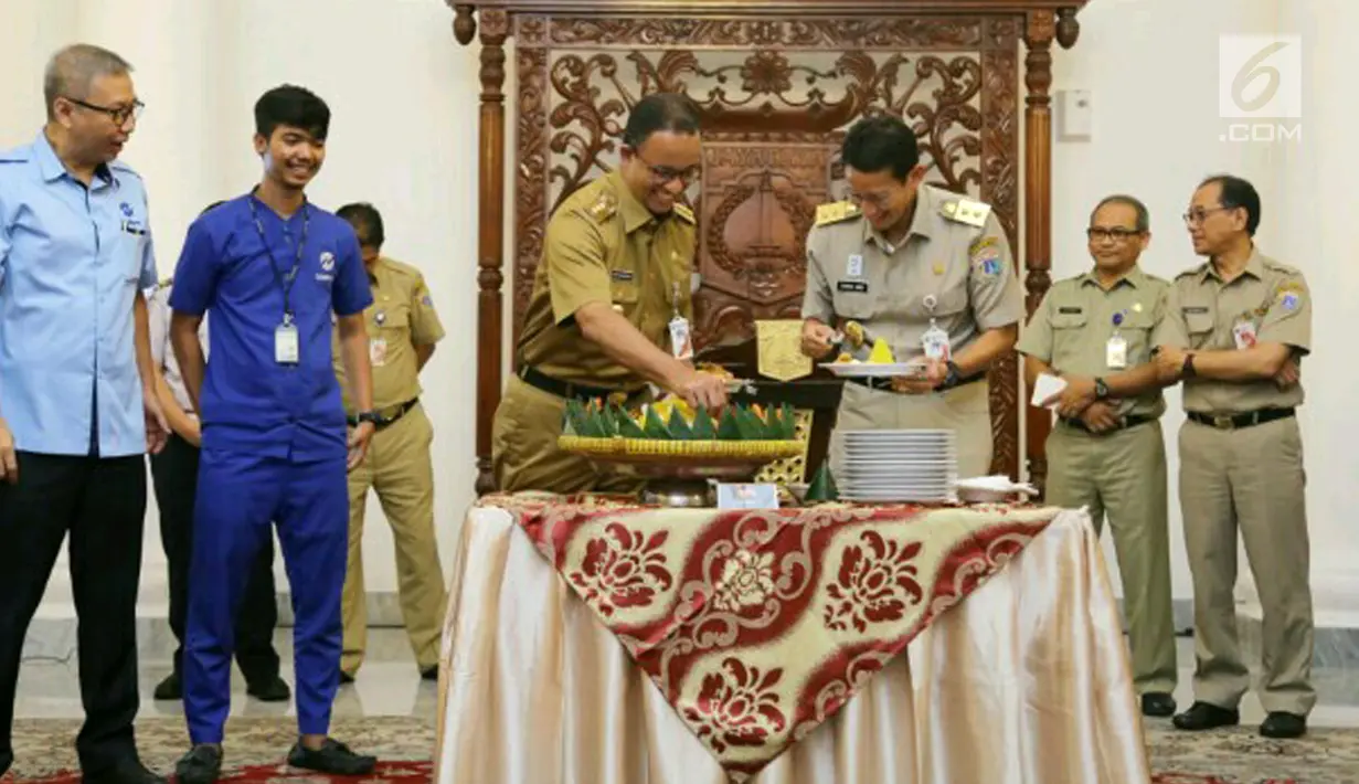 Gubernur DKI Jakarta Anies Baswedan dan Wakilnya Sandiaga Uno memotong tumpeng bersama pegawai Transjakarta, Jakarta, Selasa (20/3). Anies berharap peningkatan penumpang Transjakarta juga diimbangi oleh aspek kualitas. (Liputan6.com/Pool/Dadang WS)