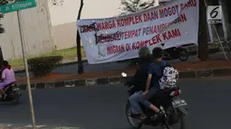 Pengendara motor melintasi spanduk penolakan lokasi penampungan pencari suaka di Kalideres, Jakarta, Selasa (16/7/2019). Sebelumnya, para pencari suaka dari berbagai negara berkonfilk ini tinggal di pinggir jalan dan trotoar di kawasan Kebon Sirih, Jakarta. (Liputan6.com/Helmi Fithriansyah)