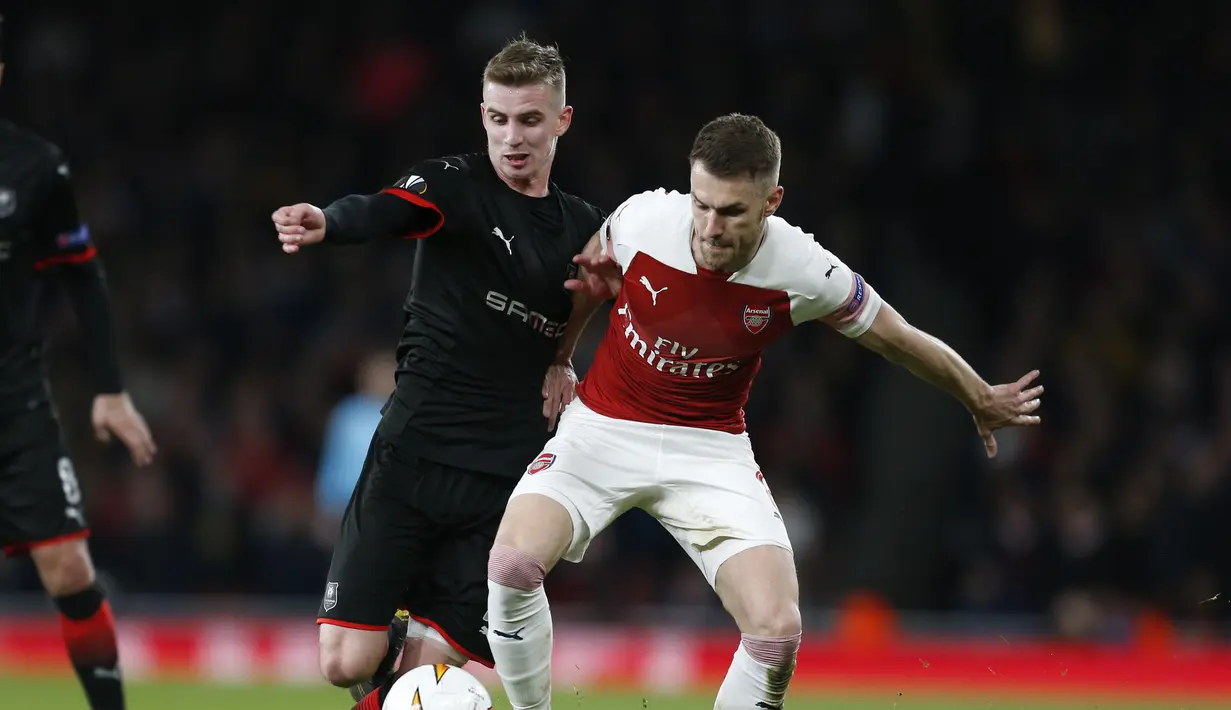 Duel antara Aaron Ramsey dan Benjamin Bourigeaud pada leg kedua,babak 16 besar Liga Europa yang berlangsung di Stadion Emirates, London, Jumat (15/3). Arsenal menang 3-0 atas Rennes. (AFP/Ian Kington)