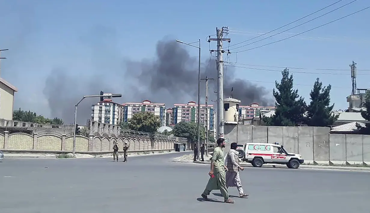 Warga berjalan ketika kepulan asap terlihat setelah ledakan besar di Kabul, Afghanistan, Senin (1/7/2019). Ledakan besar menyebabkan puluhan orang dilarikan ke rumah sakit, baik akibat terkena puing bangunan maupun asap tebal, demikian sebagaimana dikutip dari Al Jazeera pada Senin (1/7/2019). (AFP