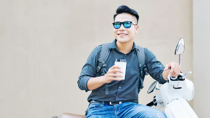 pria tersenyum pakai kacamata bersepeda motor vespa