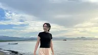 Bermain di pantai, Happy Asmara tampil dengan atasan kaos hitam ketat dipadukan celana pendek warna peach dan sandal karet putihnya.  (@happy_asmara77)