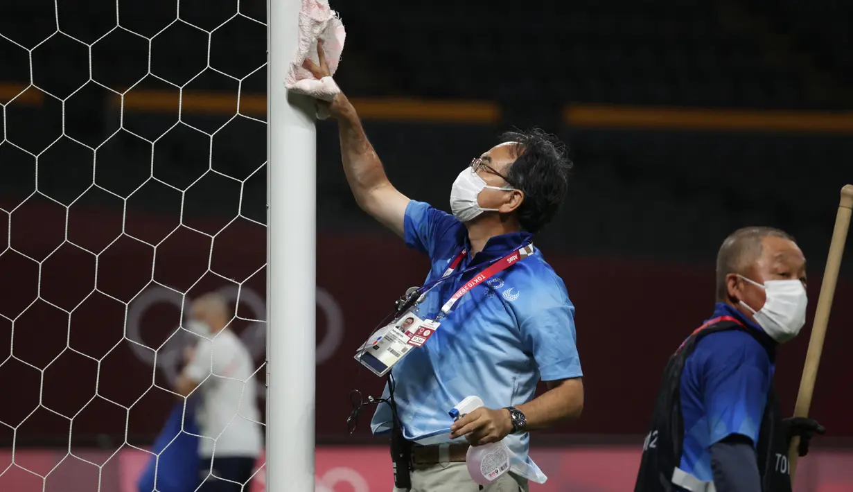Petugas mendisinfeksi tiang gawang untuk menghentikan penyebaran virus corona COVID-19 setelah pertandingan sepak bola putaran pertama grup C putra Olimpiade Tokyo 2020 antara Mesir dan Spanyol di Sapporo Dome, Sapporo, Jepang, Kamis (22/7/2021). (ASANO IKKO/AFP)