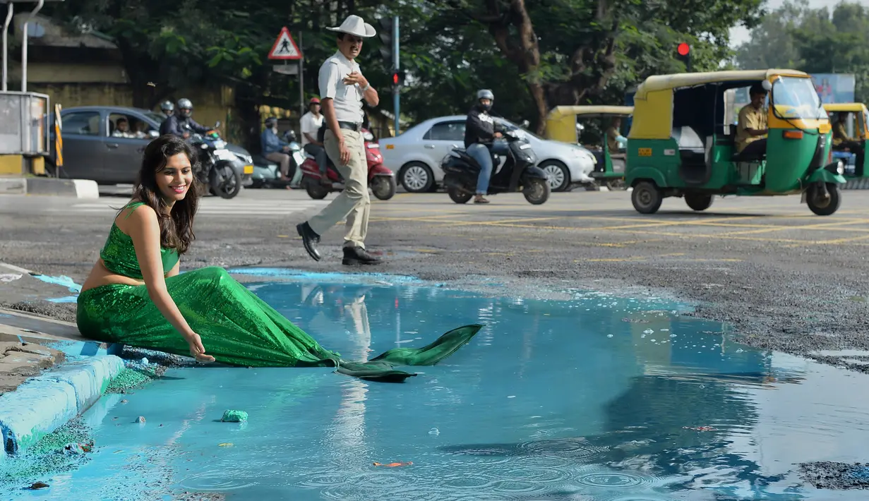 Seorang model berpakaian seperti putri duyung ambil bagian dalam seni instalasi seniman Baadal Nanjundawsamy di Bangalore, India, 13 Oktober 2107. Model itu terlihat bermain air yang telah dicampur cat air biru di tepi kubangan. (MANJUNATH KIRAN / AFP)