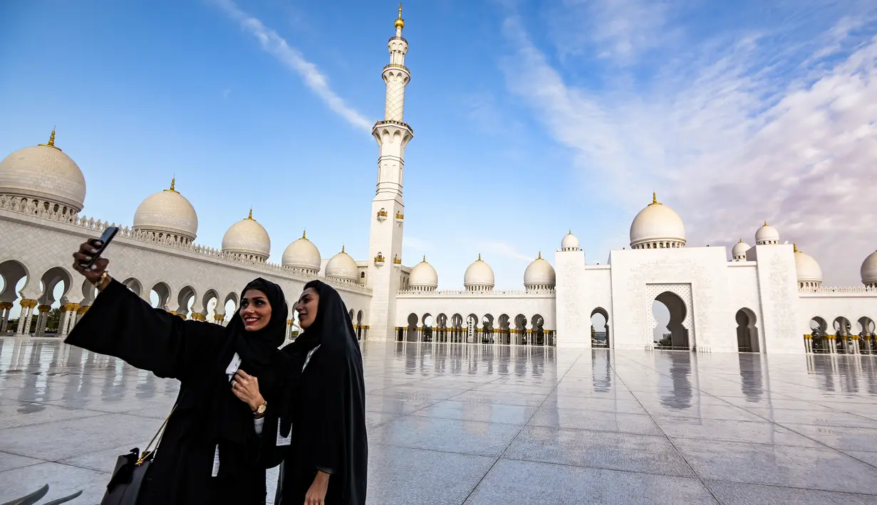 Dua wanita berswafoto dengan latar belakang halaman Masjid Agung Sheikh Zayed di Abu Dhabi, Uni Emirat Arab. Masjid ini menjadi destinasi wisata religi dan landmark yang sering didatangi selebriti, turis dan tokoh dunia. (Photo by Vincenzo PINTO / AFP)