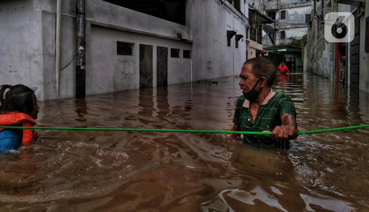 Warga berpegangan pada tali saat berjalan menyusuri banjir yang merendam permukiman di kawasan Kebalen, Jakarta, Sabtu (20/2/2021). Curah hujan yang tinggi menyebabkan banjir setinggi orang dewasa di kawasan Kebalen. (Liputan6.com/Johan Tallo)