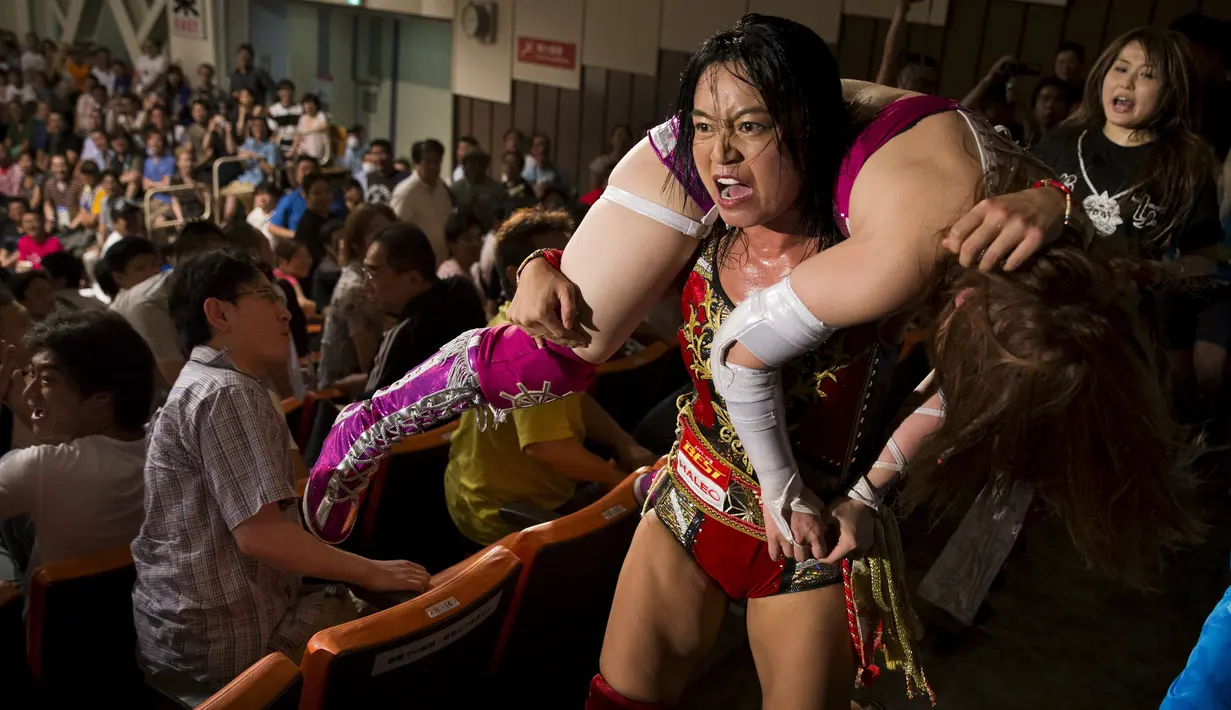 Pegulat Mieko Satomuran mengangkat lawannya Kairi Hojo melalui tribun penonton pada pertandingan gulat wanita profesional di Tokyo , Jepang , (26/7/2015).Wanita tersebut bergulat untuk mendapatkan gelar World Wonder Ring Stardom. (REUTERS / Thomas Peter)