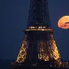 Foto yang diambil di Paris pada 23 April 2024 ini menunjukkan bulan purnama di bulan April, yang memiliki julukan pink moon atau bulan merah muda, terlihat di belakang Menara Eiffel. (Stefano RELLANDINI / AFP)
