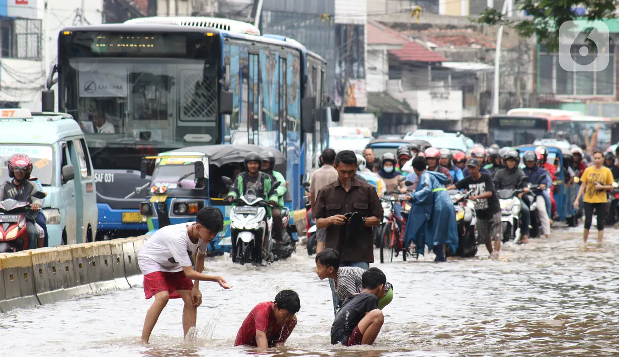 Anak-anak bermain genangan air di sebagian ruas Jalan Jatinegara Barat, Jakarta, Rabu Rabu (1/1/2020). Hujan yang mengguyur Jakarta sejak Selasa sore (31/12/2019) mengakibatkan banjir di sejumlah titik di Jakarta. (Liputan6.com/Helmi Fithriansyah)