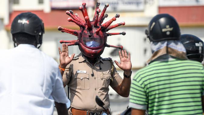 Inspektur polisi Rajesh Babu mengenakan helm berbentuk virus corona saat mengimbau pengendara motor selama lockdown di pos pemeriksaan di Chennai, India, Sabtu (28/3/2020). Cara ini bertujuan agar warga menerapkan social distancing dan tetap berada di rumah selama pandemi Covid-19. (Arun SANKAR/AFP)
