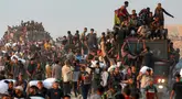 Orang-orang naik ke atas dan bergelantungan di atas truk yang mengangkut mereka, sementara yang lain berjalan sambil membawa karung-karung tepung di sepanjang jalan al-Rashid di Jabalia Barat pada 17 Juni 2025. (BASHAR TALEB/AFP)