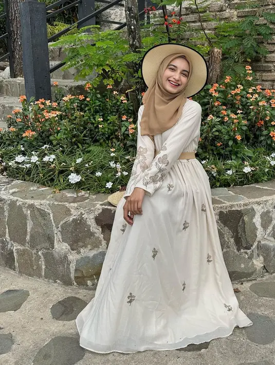 Princess look ala Cut Intan Nabila pakai dress putih dengan bordir floral yang kecil nan manis. Ia memadukan penampilannya dengan belt dan hijab cokelat, serta topi rajut serasi. [Foto: Instagram/cut.intannabila]