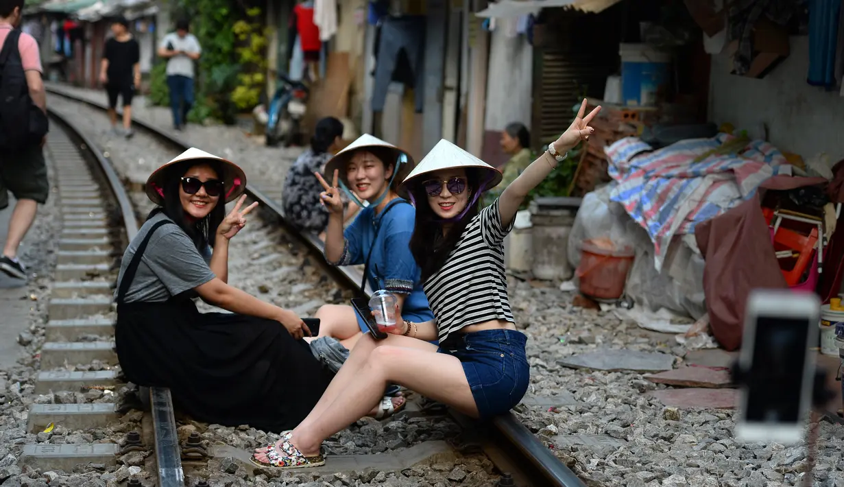 Gambar pada 21 Oktober 2018, sejumlah turis wanita duduk di atas jalur kereta api yang melintasi kawasan permukiman di Hanoi, Vietnam. Rel kereta ini menjadi titik bagi wisatawan untuk berfoto dan mengunggahnya di jejaring sosial. (Nhac NGUYEN/AFP)