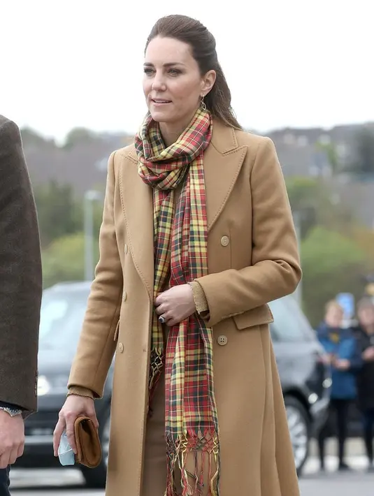 Ini saat Kate Middleton berkunjung ke Skontlandia, mengenakan long coat dari Massimo Dutti berwarna camel netral yang klasik dengan syal kotak-kotak Strathearn yang agak pop, dan celana high-waisted bernuansa senada. Foto: Bustle.