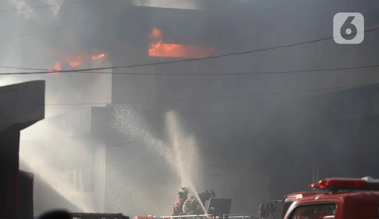 Petugas pemadam kebakaran berusaha memadamkan api yang membakar Gudang JNE Express di Jalan Pekapuran Raya, Depok, pada Senin (12/9/2022).  Besarnya api kebakaran gudang JNE pun membuat asap membumbung tinggi ke udara. (Liputan6.com/Herman Zakharia)