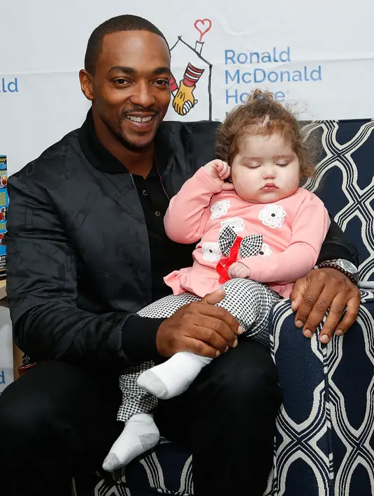 Bintang Avengers Infinity War, Anthony Mackie menggendong seorang anak wanita saat membagikan mainan di Ronald McDonald House, New York, AS, Kamis (19/4). Mainan yang dibagikan disumbangkan dari Hasbro. (LARS NIKI / GETTY IMAGES NORTH AMERICA / AFP)
