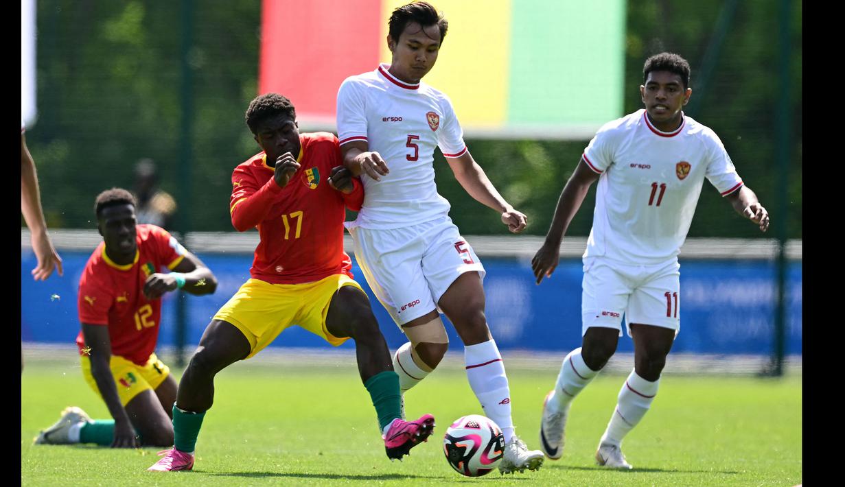 Bek Timnas Indonesia U-23, Komang Teguh (tengah) berebut bola dengan gelandang Guinea U-23, Issiaga Camara pada laga play-off antar-konfederasi menuju Olimpiade Paris 2024 di Stade Pierre Pibarot, Centre National du Football de Clairefontaine, Prancis, Kamis (9/5/2024). (AFP/Miguel Medina)
