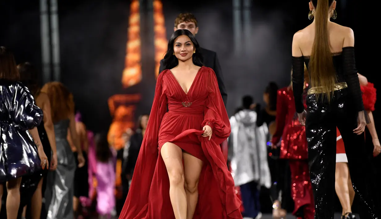 Ariel Tatum berlenggang di catwalk mengenakan kreasi untuk koleksi busana L'Oreal Spring/Summer 2023 yang disajikan selama Paris Fashion Week di Paris pada Minggu, 2 Oktober 2022. Gaun panjang itu memiliki model belahan dada rendah dan bagian rok terbuka yang mengekspos kakinya. (AFP/JULIEN DE ROSA)