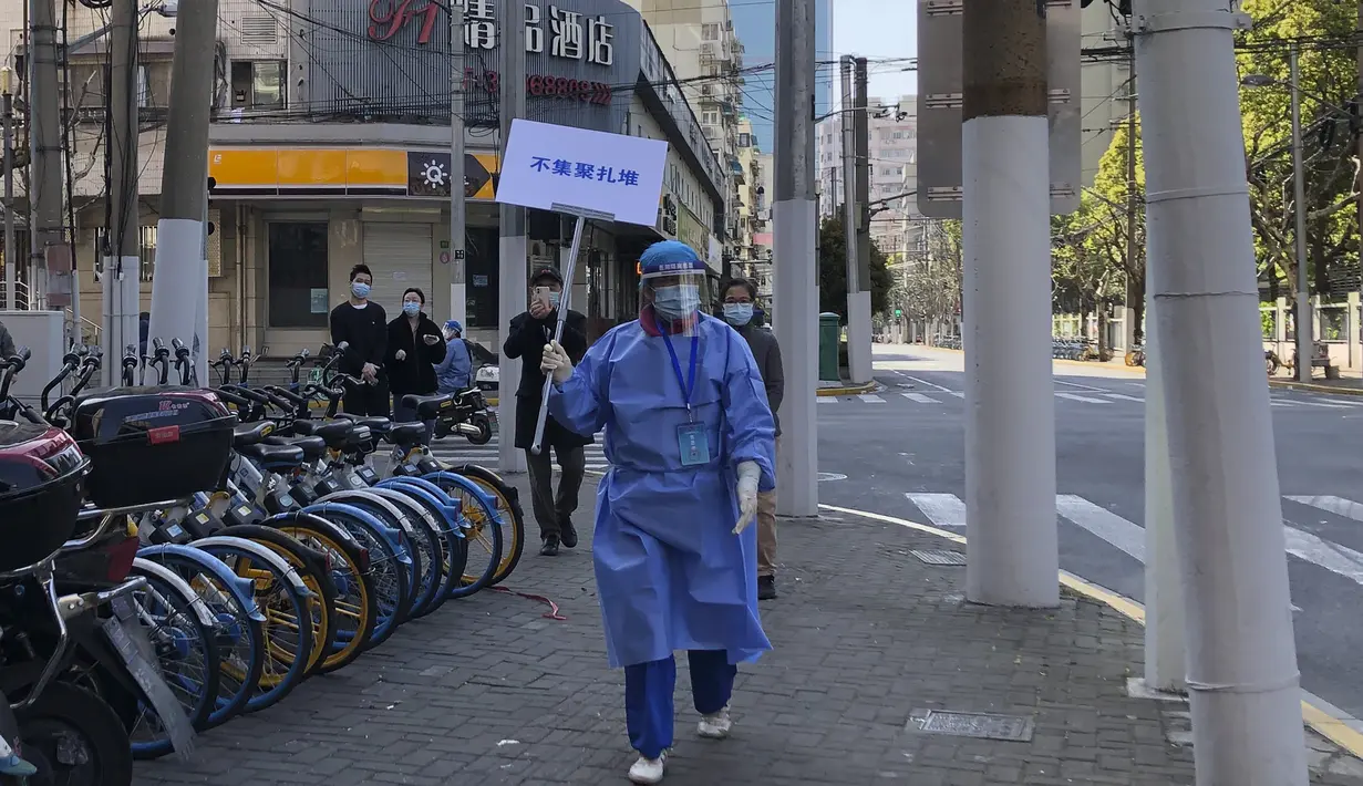 Pekerja dengan alat pelindung memegang tanda bertuliskan "Jangan berkerumun" selama hari pengujian massal bagi penduduk di distrik Jingan, Shanghai barat (4/4/2022). China telah mengirim lebih dari 10.000 petugas kesehatan ke Shanghai, termasuk 2.000 staf medis militer. (AP Photo/Chen Si)