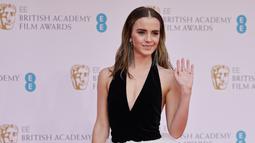 Aktris Inggris Emma Watson melambaikan tangan di karpet merah saat tiba di BAFTA British Academy Film Awards di Royal Albert Hall, di London (13/3/2022). Emma Watson melengkapi ansambel sensasionalnya dengan sepasang anting rumbai perak mewah dan serangkaian cincin perak. (AFP/Tolga Akmen)