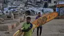 Dan, kawasan pantai di Kota Gaza menjadi salah satu sumber kebahagiaan berharga bagi warga Palestina yang ingin melepaskan diri dari tekanan situasi selama ini. Tampak dalam foto, warga Palestina, Khalil Abu Jayyab (depan) dan Tahseen Abu Assi membawa papan selancar mereka saat memasuki area sepanjang garis pantai di Kota Gaza, Minggu, 28 Desember 2025. (AP Photo/Jehad Alshrafi)