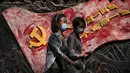 Wanita mengenakan masker wajah berjalan di dekat mural yang menggambarkan bendera partai komunis dan slogan partai di Beijing, Selasa (6/9/2022). China melarang warganya lakukan perjalanan domestik selama liburan nasional mendatang. (AP Photo/Andy Wong)