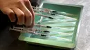 Seorang tentara Swiss menyiapkan jarum suntik dengan vaksin COVID-19 Biontech/Pfizer di Delemont, Swiss, 14 Desember 2021. Swiss yang dilanda gelombang infeksi baru COVID-19 telah memanggil tentara untuk mempercepat vaksinasi.
(Fabrice COFFRINI/AFP)