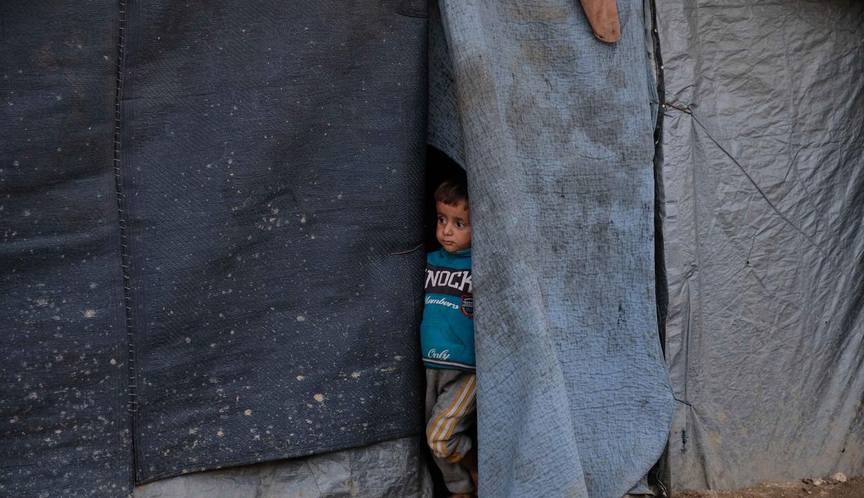 Pemerintah kota Jabalia melaporkan, sekitar 90 persen peralatan operasional untuk membersihkan puing-puing dan memulihkan infrastruktur dasar telah lumpuh atau hancur. Tampak dalam foto, seorang anak mengintip dari balik terpal di kamp pengungsian di Jabalia, di bagian utara Jalur Gaza, Minggu 7 Desember 2025. (AP Photo/Jehad Alshrafi)