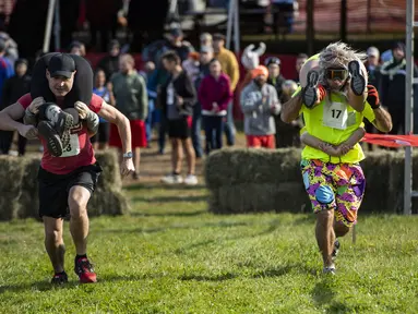 Dua tim bersaing sambil menggendong istri mereka dalam North American Wife Carrying Championship di Sunday River Resort di Newry, Maine, pada 8 Oktober 2022. Secara aturan, satu tim harus terdiri dari pria dan wanita yang telah berumur 21 tahun ke atas. (Joseph Prezioso / AFP)