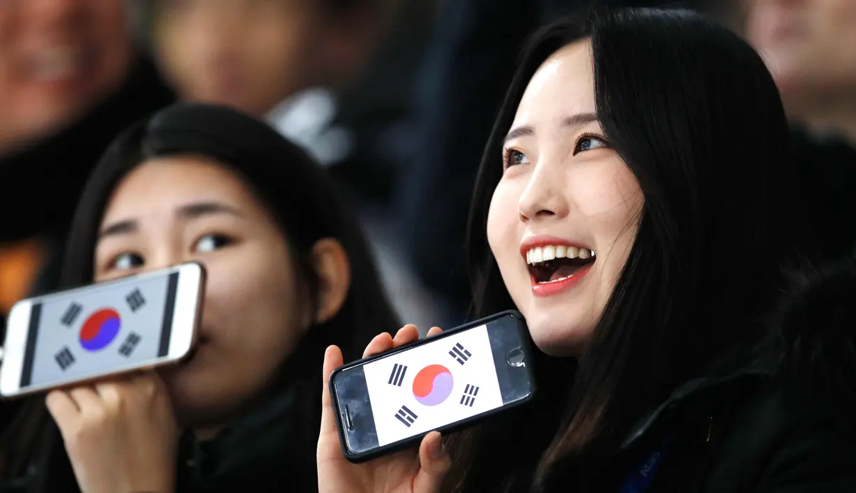 Dua wanita Fans Skating memperlihatkan ponsel mereka yang bergambar bendera Korea Selatan sebelum pertandingan balapan speed skater 1.500 meter pada Olimpiade Musim Dingin 2018 di Gangneung Oval, Korea Selatan, Selasa, (13/2). (AP Photo / Vadim Ghirda)