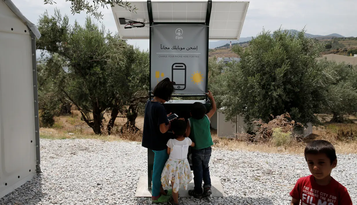 Anak-anak berdiri di dekat stasiun pengisian tenaga surya di kamp pengungsi di Pulau Lesbos, Yunani, 14 Juni 2016. Memanfaatkan teriknya matahari, stasiun pengisian baterai ponsel bertenaga surya ini bisa dinikmati pengungsi (REUTERS/Alkis Konstantinidis)