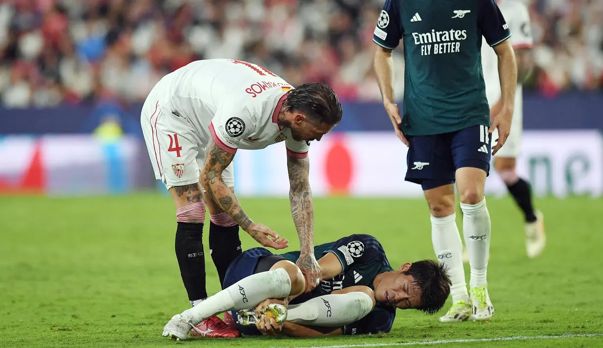 Pemain Sevilla, Sergio Ramos, berusaha membantu pemain Arsenal, Takehiro Tomiyasu, yang terjatuh pada laga Liga Champions di Stadion Ramon Sanchez Pizjuan, Rabu (25/10/2023). Berkat hasil ini, Arsenal kini berhak naik ke puncak klasemen Grup B dengan poin 6. Sementara itu, Sevilla menduduki posisi ketiga dengan perolehan poin 2. (AFP/Jorge Guerrero)