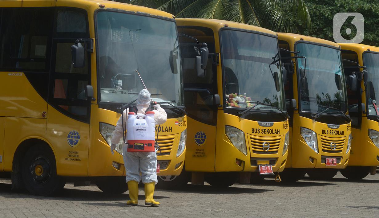 Petugas ber-APD menyemprotkan disinfektan pada bus sekolah di Posko Gabungan PSBB dan Gakplin Protkes, Puskesmas Jatinegara, Jakarta, (22/9/2020). Sejumlah unit bus sekolah kini dialihfungsikan menjadi kendaraan untuk mengantar pasien Covid-19 berstatus OTG menuju Wisma Atlet. (merdeka.com/Imam Buho
