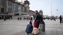 Sepasang suami istri membawa tas menunggu kereta di luar pintu masuk stasiun kereta api Beijing di ibu kota China (7/1/2023). Ketika migrasi tahunan dimulai dengan orang-orang yang kembali ke kampung halaman mereka untuk perayaan Tahun Baru Imlek. (AFP/Wang Zhao)