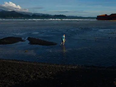 Seorang pria berjalan di pantai Lhoknga yang tercemar tumpahan batu bara dari sebuah tongkang di Aceh, Rabu (1/8). Sekitar 7.000 ton batu bara tumpah dari kapal tongkang yang kandas dihantam gelombang sehingga mencemari pantai. (AFP/CHAIDEER MAHYUDDIN)