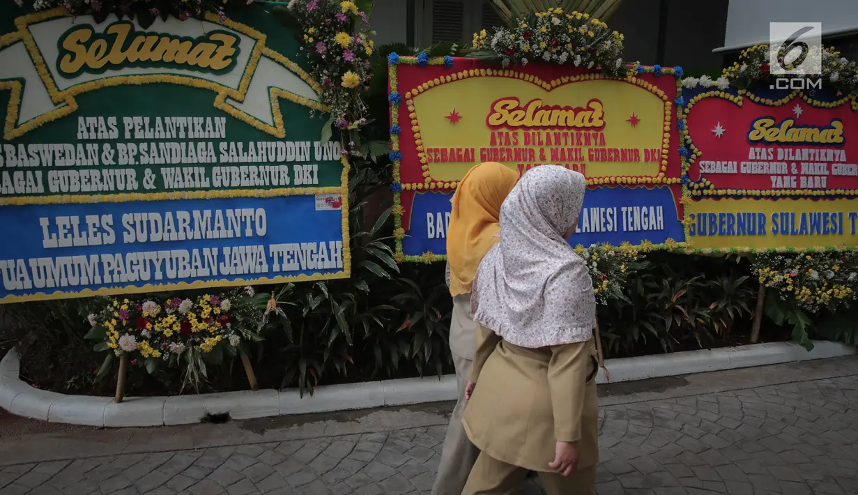 Pegawai Pemprov DKI melintasi karangan bunga untuk Gubernur dan Wakil Gubernur DKI terpilih, Anies Baswedan dan Sandiaga Uno di Halaman Balai Kota DKI Jakarta, Senin (16/10). Anies-Sandi akan dilantik Presiden di Istana Negara (Liputan6.com/Faizal Fanani)