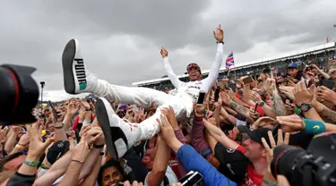 Pembalap Mercedes Lewis Hamilton melakukan selebrasi bersama penggemarnya usai berhasil memenangkan GP Inggris di sirkuit Silverstone, (16/7).  Hamilton berhasil menjuarai GP Inggris untuk kali keempat secara beruntun. (AFP Photo/Andrej Isakovic)