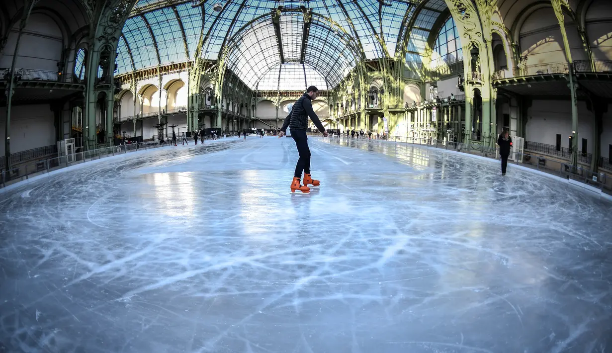 Pengunjung menikmati berseluncur di arena ice skating di bawah kubah kaca mewah legendaris, Grand Palais, Paris, Senin (17/12). Tempat seluas 1.800 meter persegi ini menjadi arena ice skating sementara terbesar di Prancis. (STEPHANE DE SAKUTIN / AFP)
