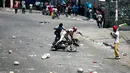 Dua pria jatuh dari sepeda motor setelah pengunjuk rasa melemparinya dengan batu karena berusaha melewati barikade yang dibuat dalam protes krisis bahan bakar di Port-au-Prince, Haiti, Senin (16/9/2019). Protes menyebabkan bank dan kantor pemerintahan tutup. (AP Photo/Dieu Nalio Chery)