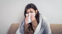 Seorang perempuan yang sedang terserang flu menyelimuti tubuhnya di atas sofa dan menutup hidungnya menggunakan tisu (Foto Dok: Freepik/pvproductions).