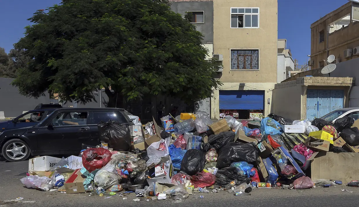 Mobil parkir di dekat tumpukan sampah di sepanjang sisi jalan di Tripoli, ibukota Libya (30/9/2019). Sampah yang berserakan di jalan tersebut menambah cobaan sehari-hari bagi penduduk ibukota yang kehidupannya telah diselingi kekurangan bahan bakar, listrik, dan air. (AFP Photo/Mahmud Turkia)