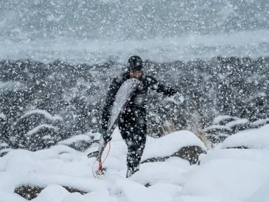 Seorang surfer atau peselancar berjalan keluar dari air di bawah hujan salju di Unstad, Norwegia Utara (11/3). Pria ini berselancar di wiliyah Lingkaran Arktik dengan suhu minus 13 derajat Celsius. (AFP Photo/Olivier Morin)