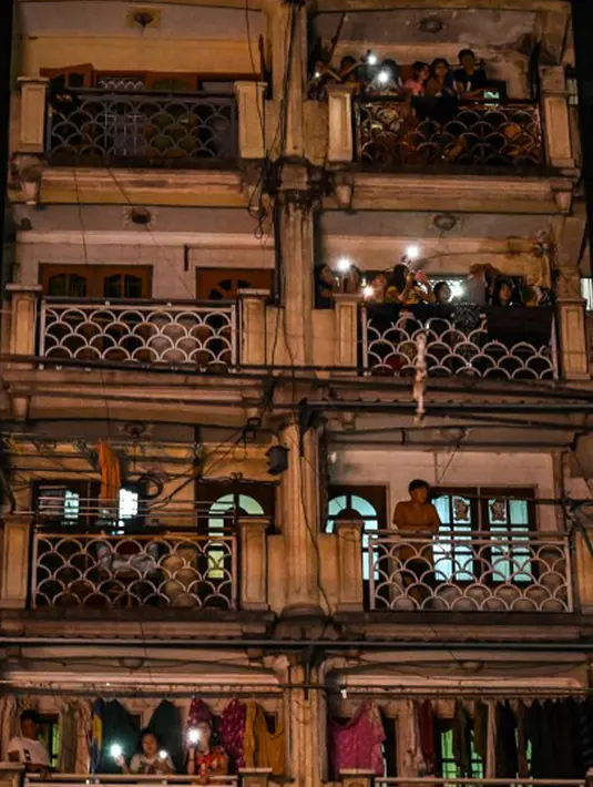 Warga menyaksikan dari gedung saat orang-orang membuat keributan dengan memukul-mukul benda setelah seruan untuk protes keluar di media sosial di Yangon, Myanmar, 3 Februari 2021. Kudeta militer Myanmar terus memicu protes warga membuat keributan. (STR/AFP)