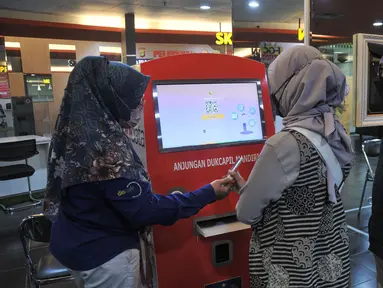 Petugas saat membantu warga yang ingin mencetak dokumen kependudukan melalui mesin Anjungan Dukcapil Mandiri (ADM) di PGC Terpadu Pelayanan Publik, Mal PGC, Cililitan, Jakarta Timur, Selasa (10/1/2023). Pemerintah Provinsi DKI Jakarta menghadirkan mesin Anjungan Dukcapil Mandiri (ADM) di 6 wilayah Ibu Kota guna memberikan kemudahan bagi masyarakat untuk menyetak dokumen kependudukan. (Merdeka.com/Iqbal S. Nugroho)