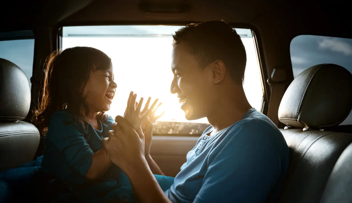 Seorang anak dan ayah sedang bermain di dalam mobil, terlihat mereka berdua tersenyum lebar dan begitu bahagia yang menggambarkan kedekatan mereka. (Odua Images/ Shutterstock.com)