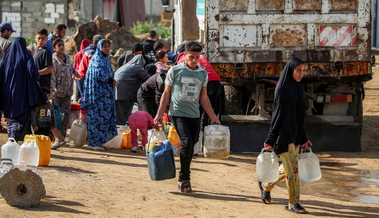 Lebih lanjut pihak OCHA mengatakan, untuk mengatasi kekurangan ini, kami bersama para mitra telah meningkatkan produksi air dan menyalurkan pengiriman melalui truk dari sumur-sumur air tanah dan instalasi desalinasi sektor swasta. Tampak dalam foto, warga mengisi wadah air dari tangki air portabel di kamp pengungsi Palestina Maghazi, Jalur Gaza tengah pada Rabu 11 Februari 2026. (Eyad BABA/AFP)