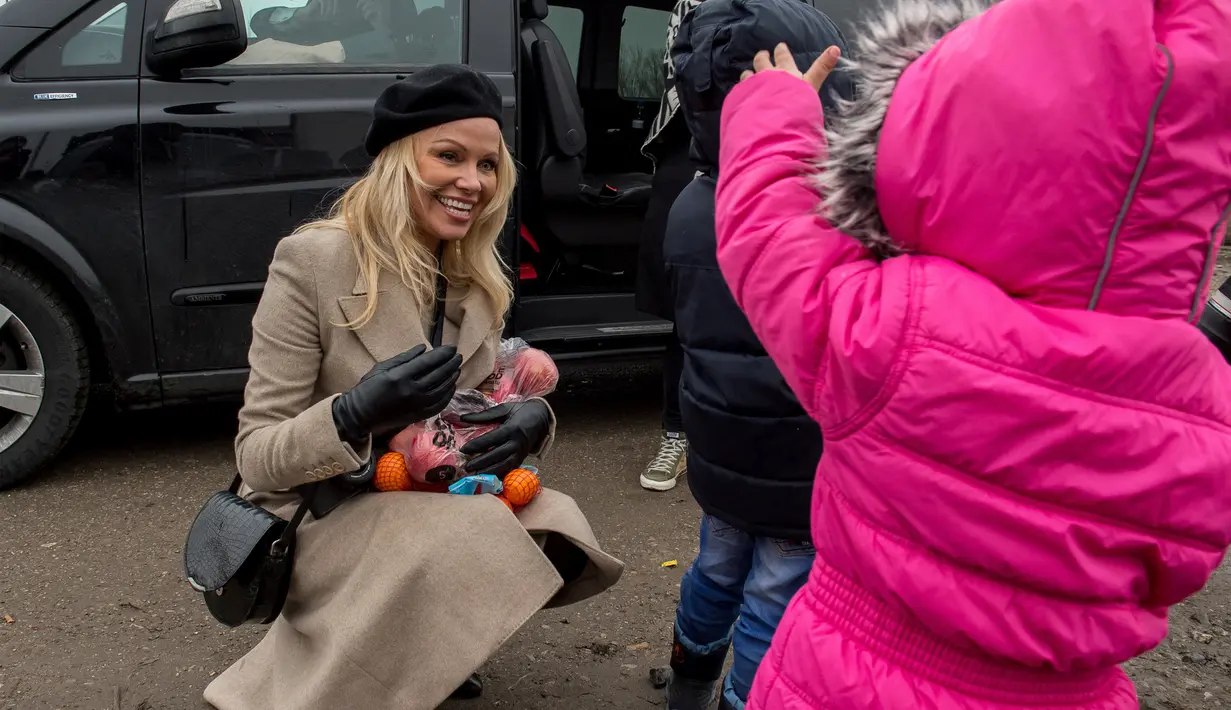 Aktris asal Kanada, Pamela Anderson memberikan buah-buahan kepada seorang anak di pengungsian Grande-Synthe, Prancis (25/1). Dalam kunjungannya, Pamela menyumbangkan buku anak-anak, makanan serta perlengkapan lainnya. (AFP/Philippe Huguen)