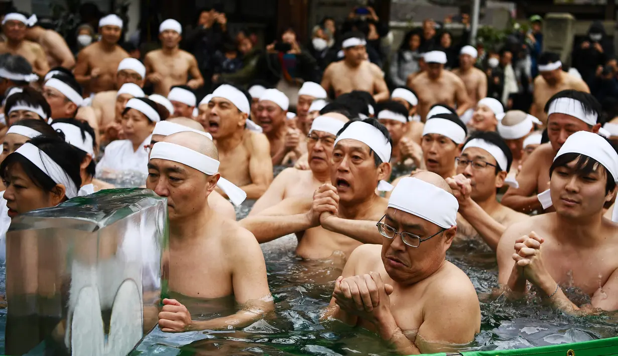 Orang-orang percaya Shinto dari Kuil Teppozu Inari mandi dengan air dingin untuk menyucikan jiwa dan tubuh mereka selama ritual Tahun Baru di Tokyo, Minggu (12/1/2020). Sekitar 100 orang percaya Shinto ambil bagian dalam ritual tahunan tersebut. (AFP/Charly Triballeau)